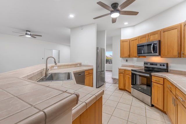 kitchen with ceiling fan, stainless steel appliances, tile counters, and sink