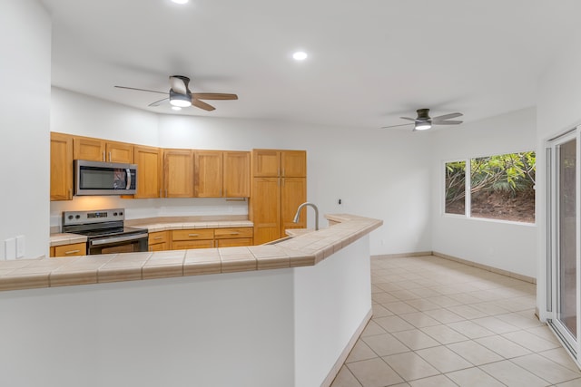 kitchen with tile countertops, sink, ceiling fan, appliances with stainless steel finishes, and kitchen peninsula