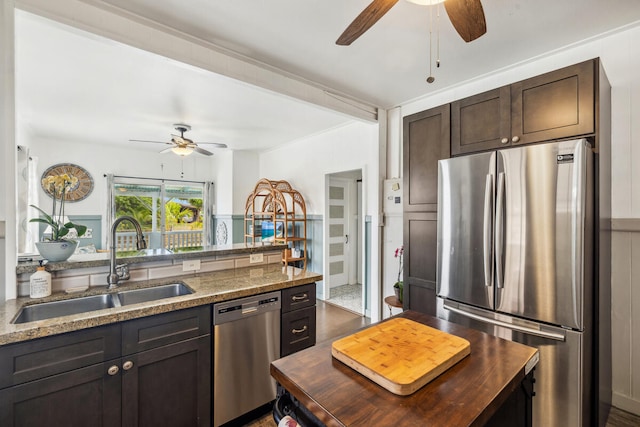 kitchen with dark brown cabinets, sink, appliances with stainless steel finishes, dark stone countertops, and ceiling fan