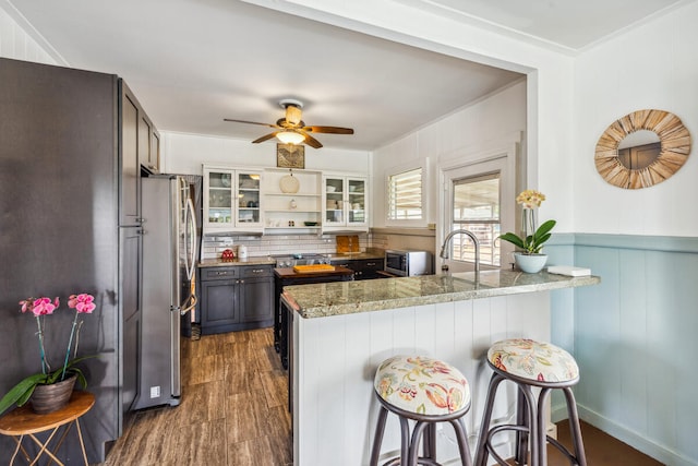 kitchen featuring light stone counters, dark wood-type flooring, kitchen peninsula, decorative backsplash, and stainless steel fridge