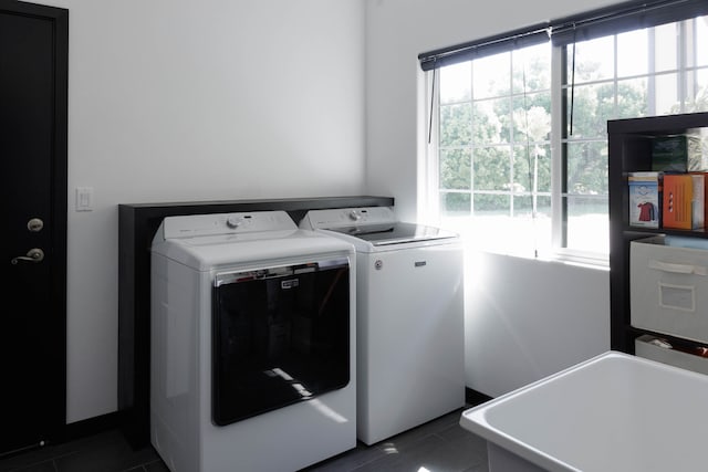 clothes washing area with a healthy amount of sunlight, independent washer and dryer, and dark tile patterned floors