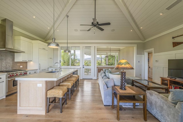 kitchen with stainless steel stove, light countertops, open floor plan, a sink, and wall chimney exhaust hood