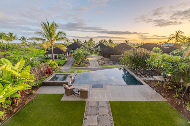 pool at dusk featuring an in ground hot tub, a lawn, and a patio