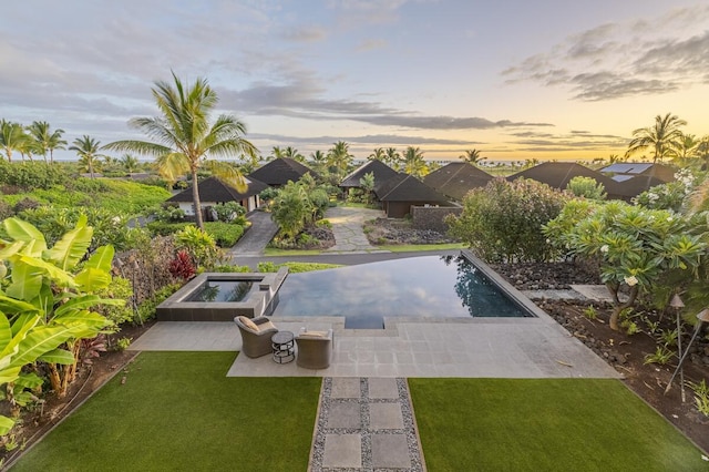 pool at dusk with an in ground hot tub, a lawn, a patio area, and an outdoor pool