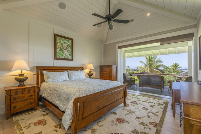 bedroom featuring lofted ceiling with beams, ceiling fan, wood finished floors, access to exterior, and a decorative wall