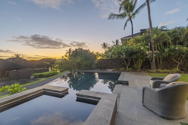 pool at dusk with an outdoor pool and a patio