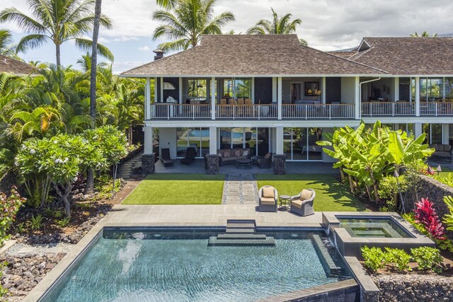 rear view of house featuring a balcony, a lawn, a patio, and a pool with hot tub