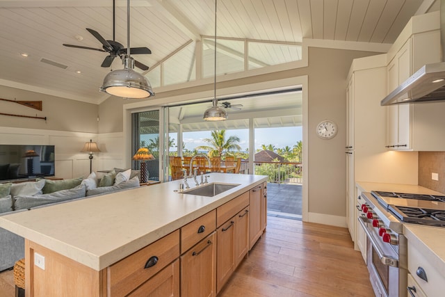 kitchen with range with two ovens, an island with sink, sink, ceiling fan, and wall chimney range hood