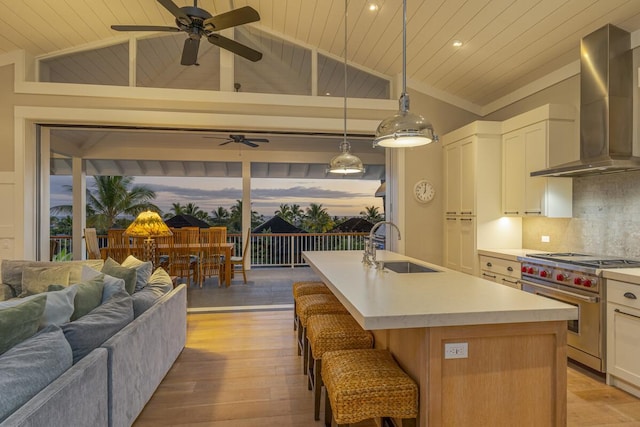 kitchen featuring a center island with sink, light hardwood / wood-style flooring, ceiling fan, premium range, and wall chimney range hood