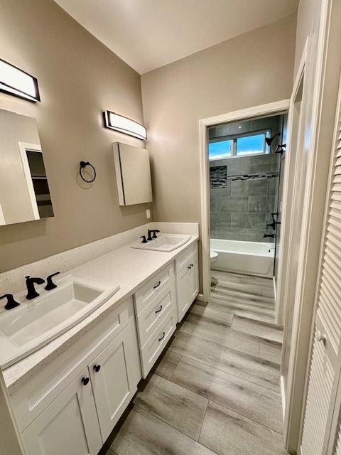 bathroom with toilet, wood finished floors, a sink, shower / washtub combination, and double vanity