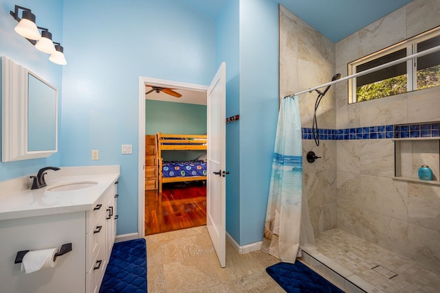 full bathroom with a ceiling fan, tiled shower, vanity, and baseboards
