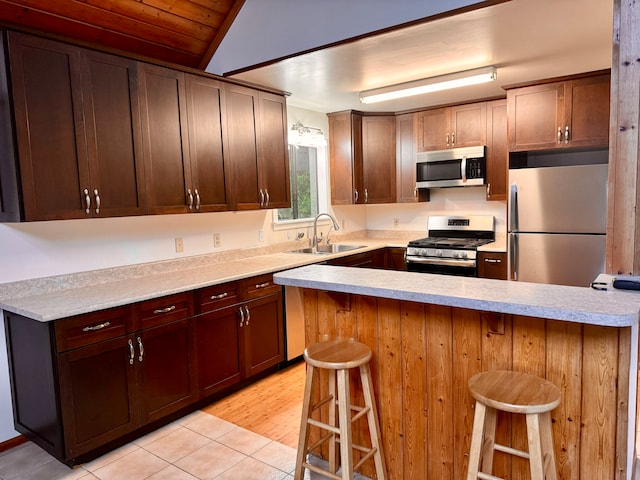 kitchen with vaulted ceiling, light hardwood / wood-style flooring, a kitchen bar, stainless steel appliances, and sink