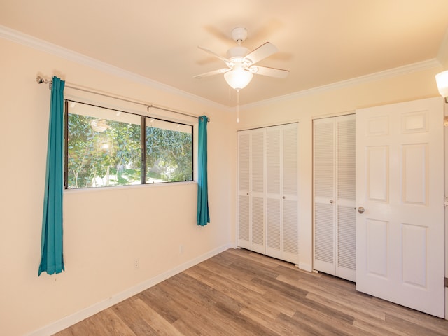 unfurnished bedroom with light hardwood / wood-style flooring, ceiling fan, crown molding, and multiple closets