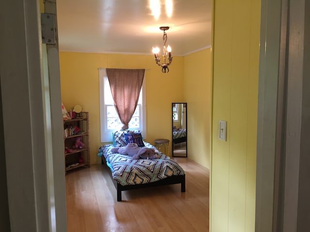 bedroom with an inviting chandelier, wood-type flooring, and ornamental molding