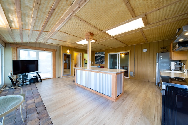 kitchen with sink, wood walls, vaulted ceiling, light hardwood / wood-style flooring, and extractor fan