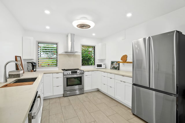 kitchen featuring sink, wall chimney range hood, appliances with stainless steel finishes, and white cabinets