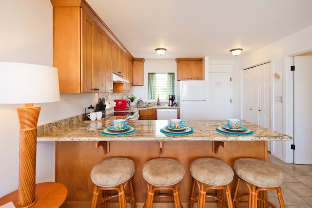 kitchen featuring white appliances, kitchen peninsula, a breakfast bar area, and light stone countertops