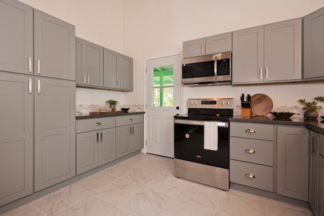 kitchen featuring gray cabinetry, a towering ceiling, and appliances with stainless steel finishes