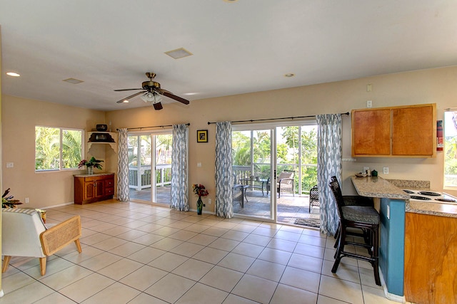 kitchen with white electric stovetop, light tile patterned flooring, light stone countertops, and ceiling fan