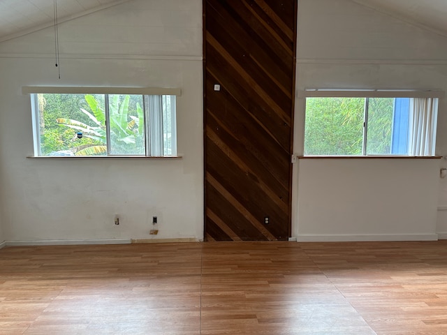 empty room featuring plenty of natural light, vaulted ceiling, wood walls, and light hardwood / wood-style flooring