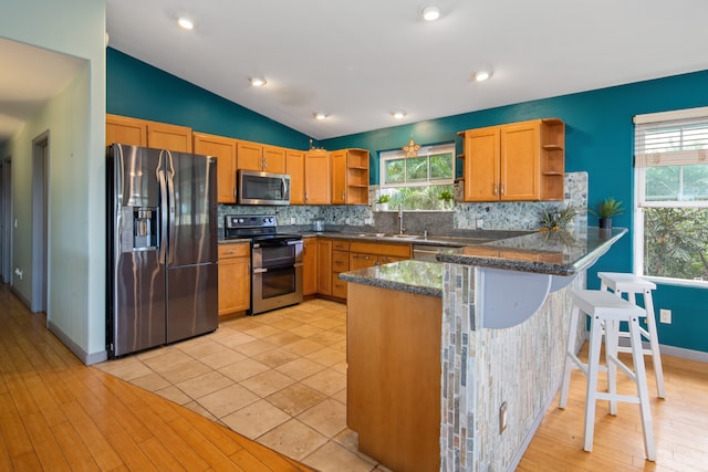 kitchen featuring light wood-type flooring, stainless steel appliances, kitchen peninsula, decorative backsplash, and vaulted ceiling