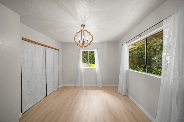 unfurnished bedroom featuring a textured ceiling, light hardwood / wood-style flooring, a closet, and a notable chandelier