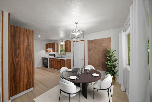 dining area featuring an inviting chandelier, sink, light hardwood / wood-style floors, and a textured ceiling