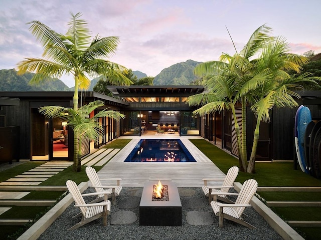 back house at dusk featuring an outdoor fire pit, a mountain view, a yard, and a patio