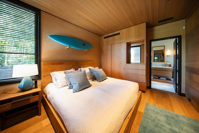 bedroom with wood walls, ensuite bath, and light hardwood / wood-style flooring