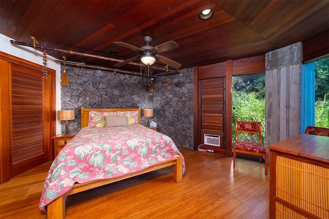 bedroom with ceiling fan, a wall unit AC, hardwood / wood-style floors, and wooden ceiling