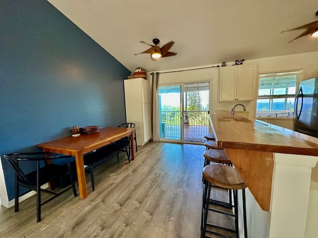 kitchen with vaulted ceiling, light wood-type flooring, kitchen peninsula, ceiling fan, and a breakfast bar