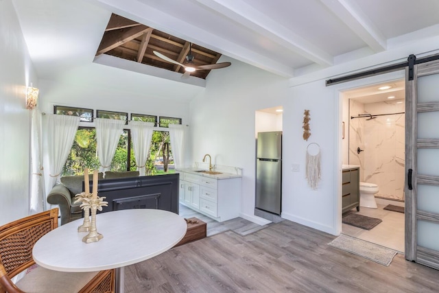 dining room with a barn door, sink, light hardwood / wood-style floors, and vaulted ceiling with beams