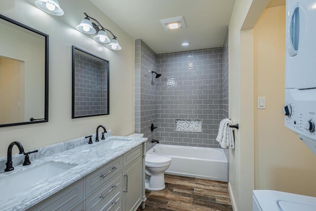 full bathroom with vanity, hardwood / wood-style flooring, tiled shower / bath combo, toilet, and stacked washing maching and dryer