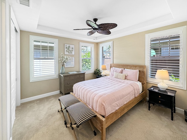 carpeted bedroom with a raised ceiling and ceiling fan