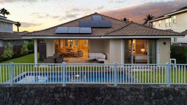 back house at dusk featuring a lawn, solar panels, an outdoor living space, a fenced in pool, and a patio area