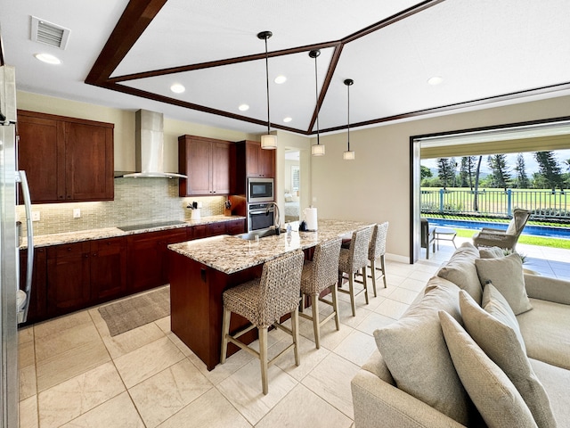 kitchen with a center island with sink, a kitchen breakfast bar, wall chimney range hood, light stone countertops, and stainless steel appliances