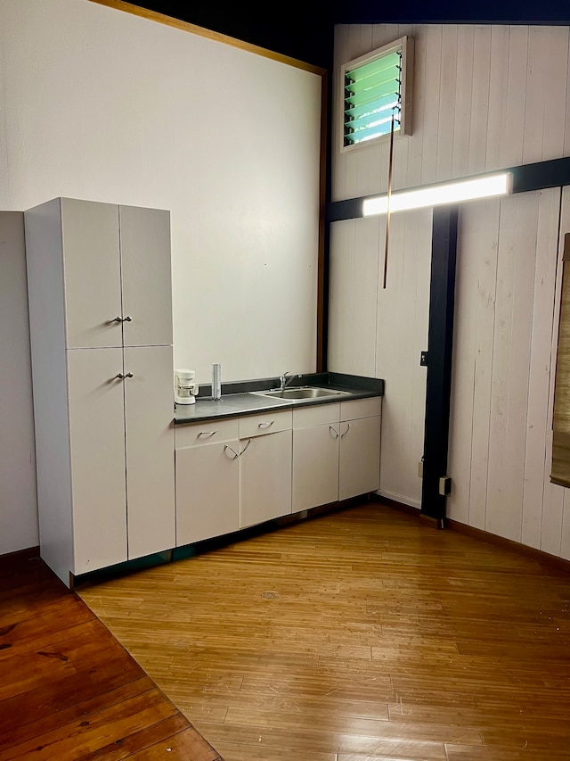 kitchen with light hardwood / wood-style floors, wooden walls, and sink