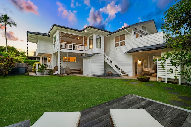 back house at dusk with a balcony, a yard, and a patio area