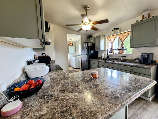 kitchen with independent washer and dryer, light hardwood / wood-style floors, sink, black refrigerator, and ceiling fan