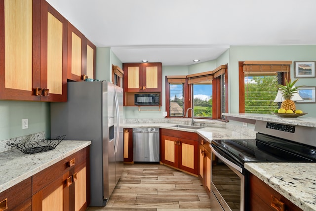 kitchen featuring appliances with stainless steel finishes, light stone countertops, sink, and light wood-type flooring