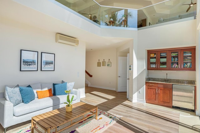 living room featuring a wall mounted air conditioner, a towering ceiling, light hardwood / wood-style floors, and indoor bar