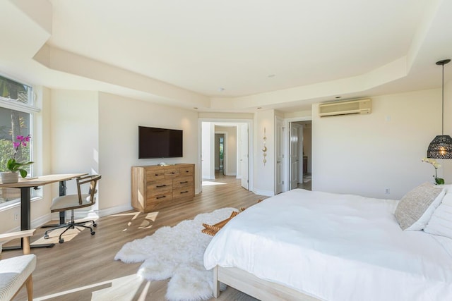 bedroom featuring a raised ceiling, a wall mounted AC, and light wood-type flooring