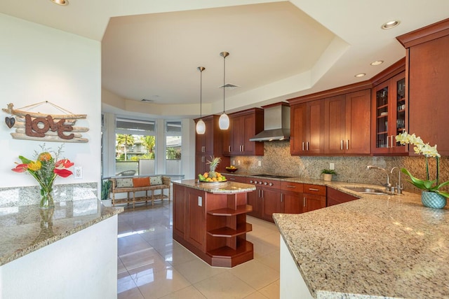 kitchen featuring sink, a kitchen island, pendant lighting, decorative backsplash, and wall chimney range hood