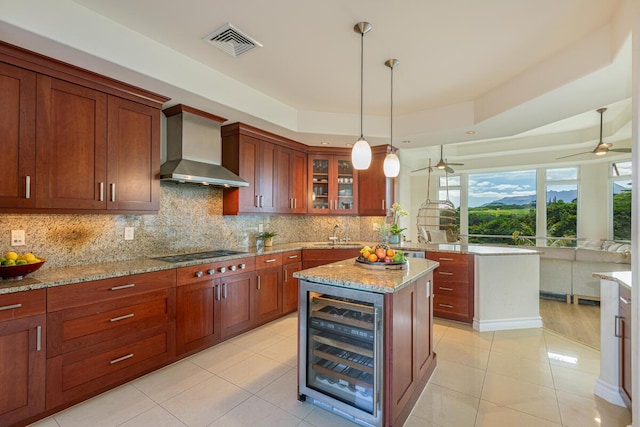 kitchen with beverage cooler, hanging light fixtures, cooktop, a raised ceiling, and wall chimney range hood