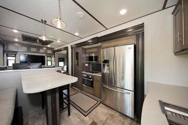 kitchen featuring stainless steel appliances, a kitchen bar, dark brown cabinets, ceiling fan, and decorative light fixtures