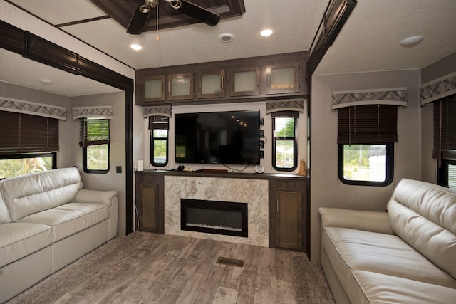 living room with ceiling fan, a textured ceiling, a fireplace, and wood-type flooring