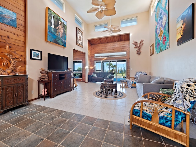 living room with ceiling fan, wooden walls, a high ceiling, and tile patterned floors