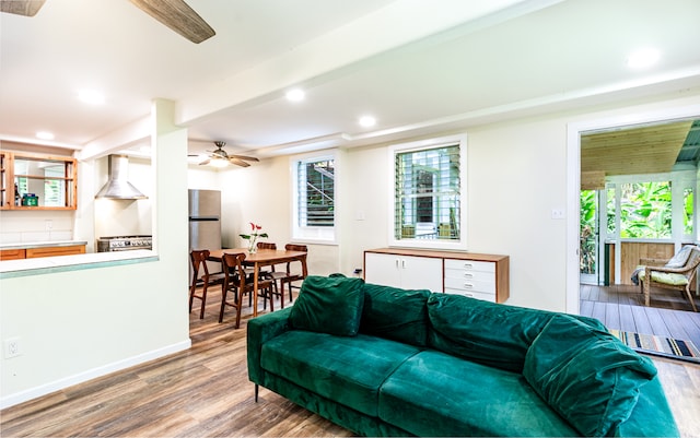 living room featuring a healthy amount of sunlight, beamed ceiling, ceiling fan, and hardwood / wood-style flooring