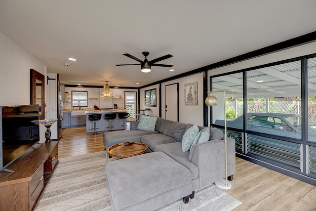 living room featuring light wood-type flooring, ceiling fan with notable chandelier, crown molding, and sink