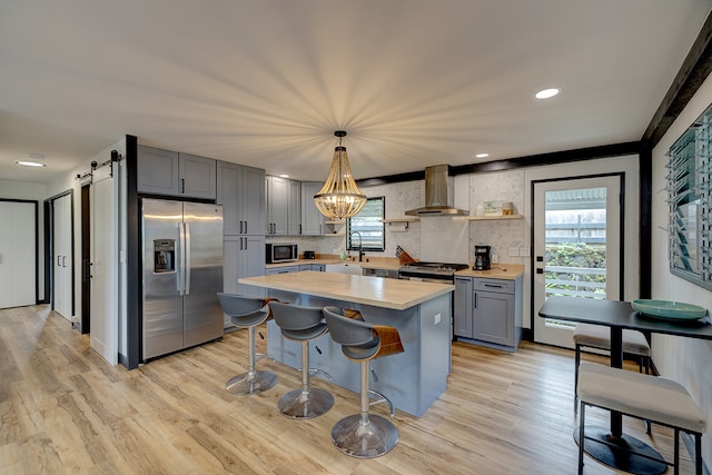 kitchen with a wealth of natural light, appliances with stainless steel finishes, wall chimney range hood, and a barn door